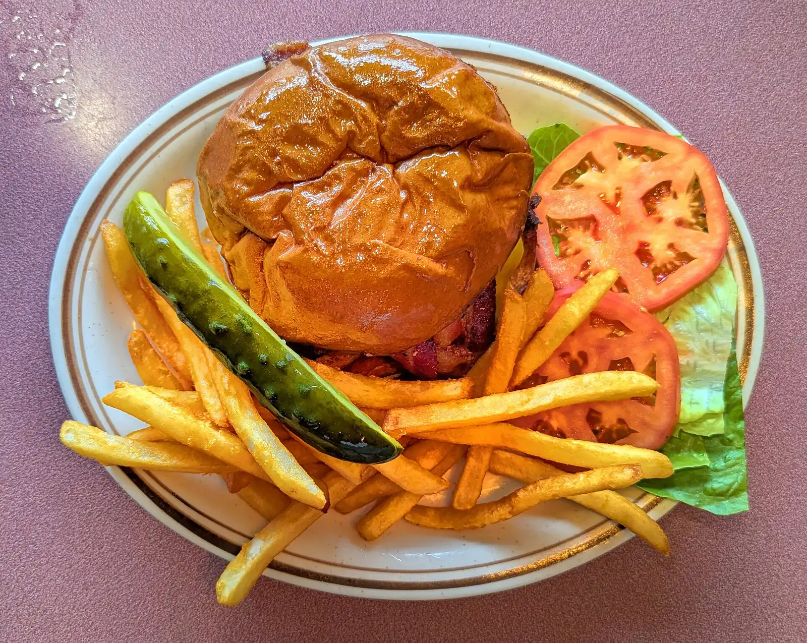 A bacon cheeseburger with fries and a pickle. The photo was not taken in Atlanta.